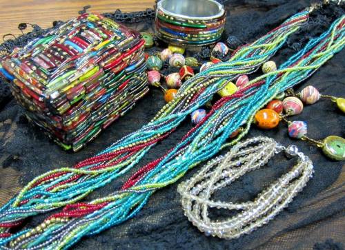 Colorful handmade jewelry and accessories displayed on a black fabric background, including beaded necklaces and a bracelet.