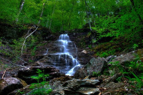 A serene waterfall cascading down rocky terrain, surrounded by lush green foliage and trees.