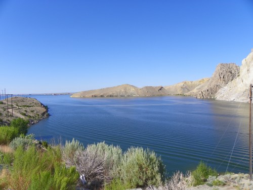 A serene lake surrounded by rocky hills and greenery under a clear blue sky.