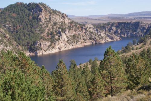 A serene landscape featuring a winding river surrounded by rocky cliffs and lush green trees under a clear blue sky.