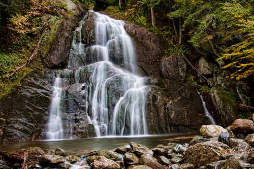 A serene waterfall cascading over rocks, surrounded by lush greenery and autumn foliage.