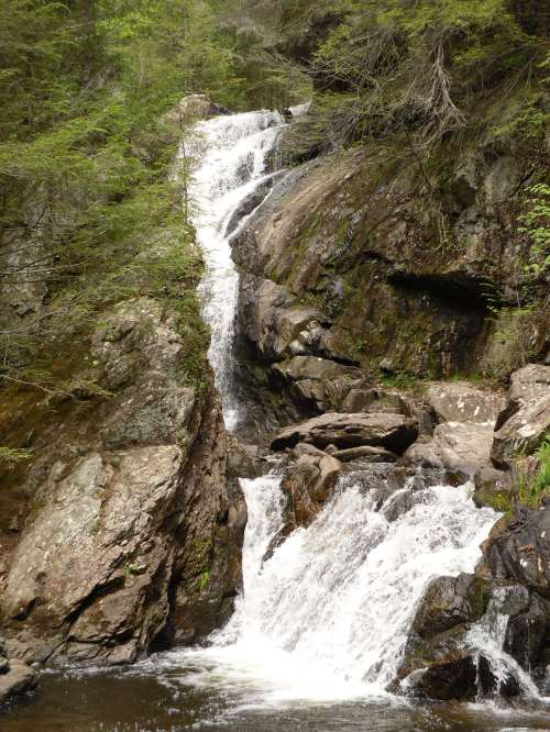 A cascading waterfall flows over rocky terrain, surrounded by lush green foliage.