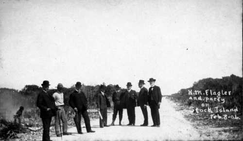 A group of men in formal attire stands on a dirt path, with trees and brush in the background, dated February 8, 1904.