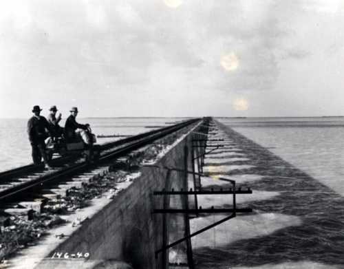 Black and white photo of workers on a railway bridge over water, with tracks extending into the distance.