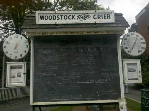 A chalkboard sign displaying community announcements, with clocks on either side, located in Woodstock.