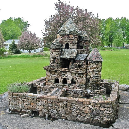 A unique stone structure resembling a small house, surrounded by grass and trees in a park-like setting.