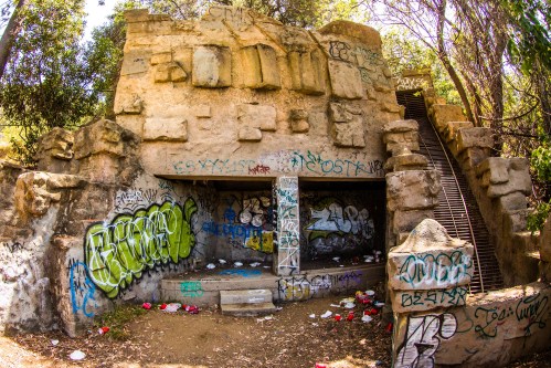 Abandoned structure covered in graffiti, surrounded by trees, with a staircase leading up on one side.