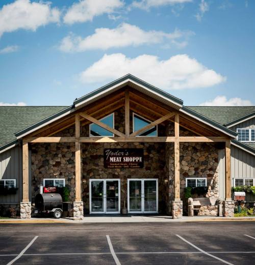 A rustic meat shop with a stone facade and wooden beams, set against a blue sky with fluffy clouds.