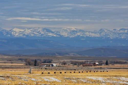 A scenic view of snow-capped mountains in the background, with a rural landscape and farm buildings in the foreground.