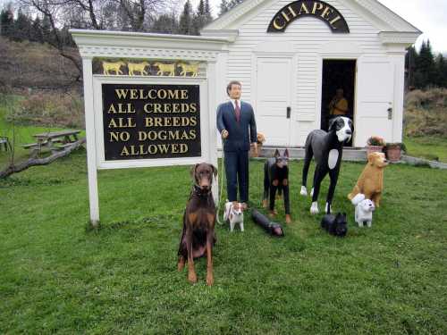 A sign outside a chapel reads "Welcome All Creeds, All Breeds, No Dogmas Allowed," with various dog statues and a figure.