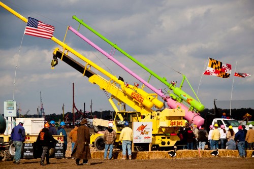 Colorful carnival catapults with flags, set against a cloudy sky, as spectators gather in a field.