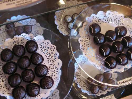 Assorted chocolate truffles arranged on lace doilies in a display case.