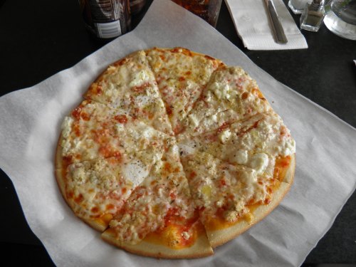 A round pizza with a golden crust, topped with cheese and a light tomato sauce, cut into slices on a white paper.