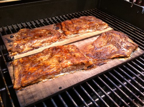 Grilled salmon fillets on cedar planks, sizzling on a barbecue grill.