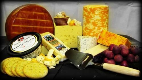 A variety of cheeses, crackers, and grapes arranged on a black surface, with a cheese knife included.