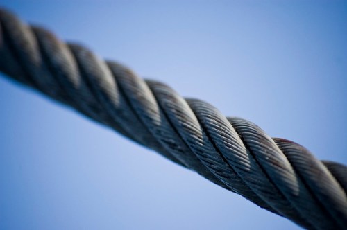 Close-up of a twisted metal cable against a blue sky background.