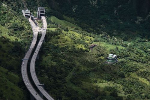 Aerial view of a winding highway surrounded by lush green hills and a small building in the foreground.