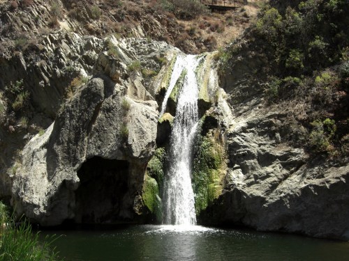 A serene waterfall cascading over rocky cliffs into a calm pool surrounded by lush greenery.