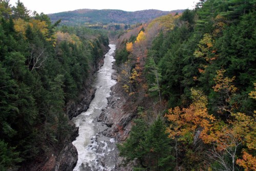 A winding river flows through a rocky gorge, surrounded by trees with autumn foliage in vibrant colors.