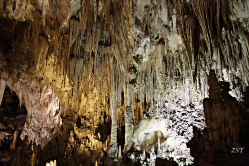 Stalactites and rock formations in a dimly lit cave, showcasing natural textures and colors.