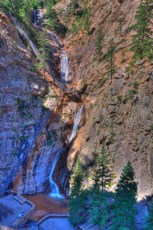 A scenic view of a waterfall cascading down rocky cliffs, surrounded by trees and wooden pathways.