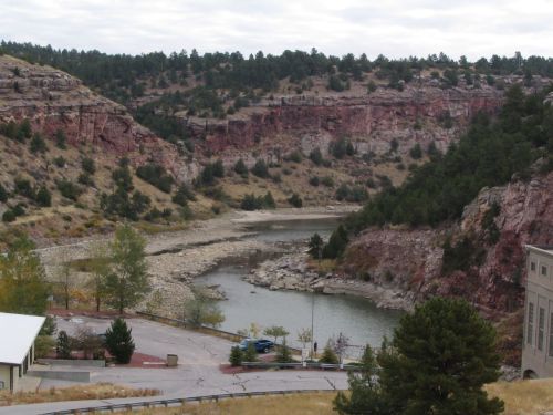 A scenic view of a river winding through rocky cliffs and greenery under a cloudy sky.