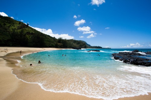 A serene beach with clear turquoise water, gentle waves, and people enjoying the sun under a bright blue sky.