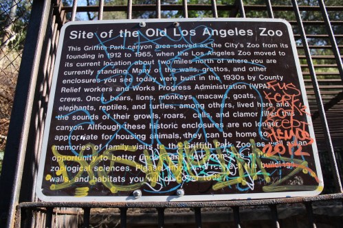 Sign about the old Los Angeles Zoo, detailing its history and closure, with graffiti and wear visible on the surface.
