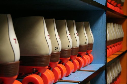 A row of vintage roller skates on a shelf, featuring orange wheels and numbered tags.