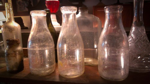 A collection of vintage glass bottles of various shapes and sizes, some clear and others tinted, on a wooden surface.