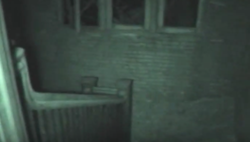 Dimly lit interior of an abandoned building, featuring a staircase and brick walls. Shadows create an eerie atmosphere.