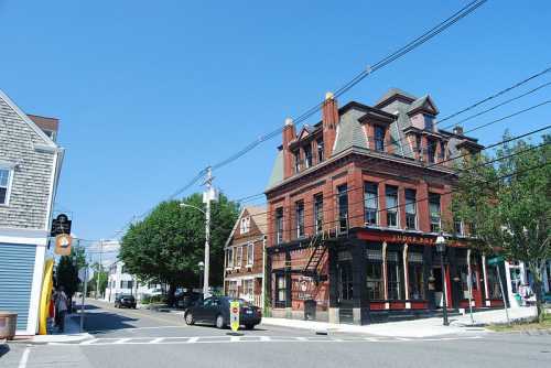 A historic red brick building at a street corner, with clear blue skies and trees in the background.