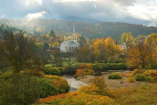 A serene landscape featuring a church, colorful autumn trees, and a winding stream under a cloudy sky.