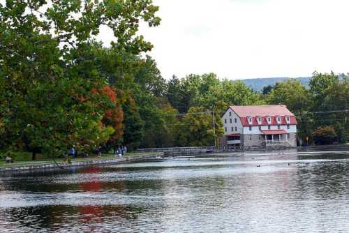 A serene lake scene with a stone building, surrounded by trees and people walking along the shore.