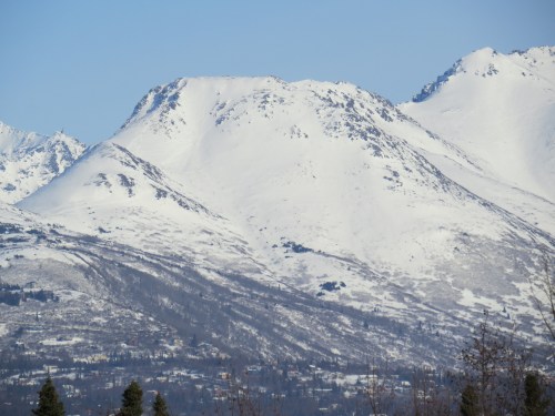 Snow-covered mountains under a clear blue sky, showcasing rugged peaks and a serene winter landscape.