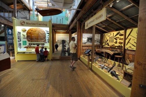 A museum interior showcasing marine carving and maritime trades, with visitors exploring exhibits and displays.