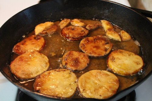 Sliced vegetables frying in a cast iron skillet, golden brown and bubbling in oil.