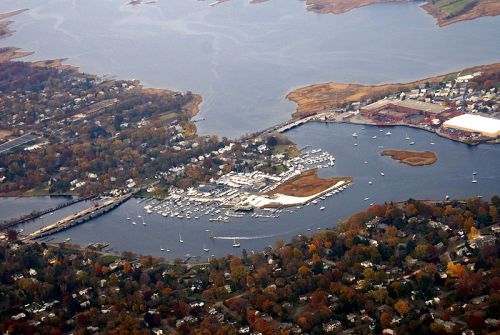 Aerial view of a marina surrounded by water, boats, and autumn-colored trees along the shoreline.