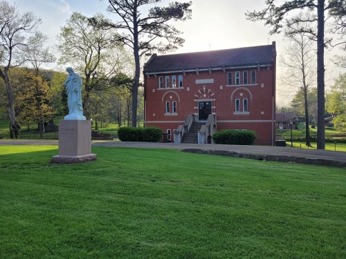 A brick building with stairs, surrounded by greenery, and a statue of a figure in the foreground.
