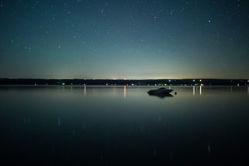 A serene night scene of a calm lake reflecting stars, with a lone boat floating peacefully on the water.