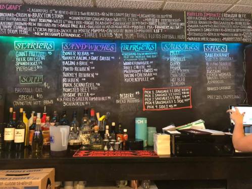 Menu board featuring starters, sandwiches, burgers, and sausages, with a selection of drinks displayed below.