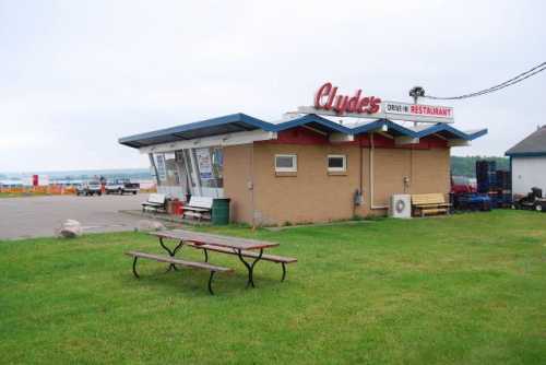 A small, retro-style drive-in restaurant named "Clyde's" with a picnic table in front and a scenic view in the background.