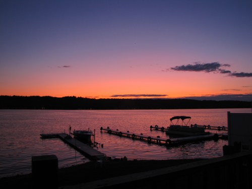 A serene lake at sunset, with boats docked and a colorful sky reflecting on the water.