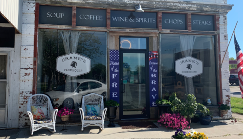 Exterior of Crane's Farmhouse, featuring a welcoming entrance, flower planters, and signs for soup, coffee, and steaks.