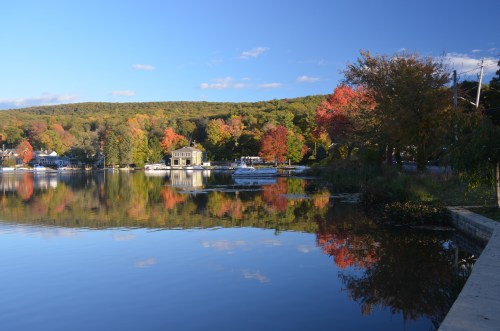 A serene lake scene with colorful autumn trees reflecting on the water under a clear blue sky.
