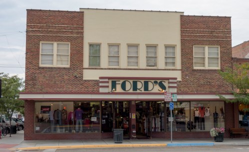 A brick storefront with large windows displaying clothing, featuring a sign that reads "FORD'S."