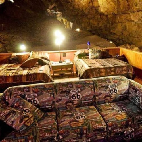 Cozy cave hotel room with two beds, a patterned couch, and warm lighting, featuring Route 66 decor.