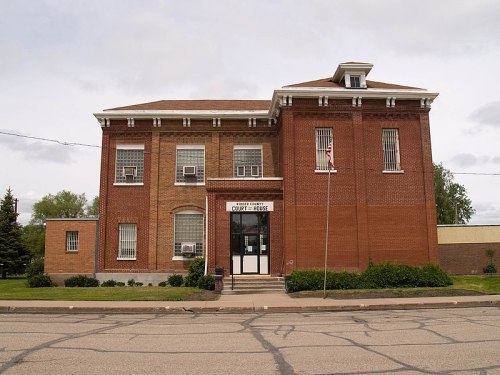 Historic brick courthouse building with large windows and a flagpole, set against a cloudy sky.