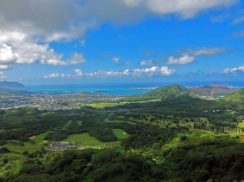A panoramic view of lush green hills and a blue ocean under a partly cloudy sky.