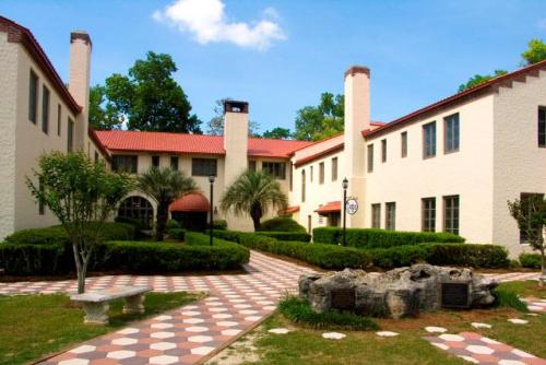 A courtyard view of a two-story building with a red tile roof, surrounded by greenery and a patterned walkway.